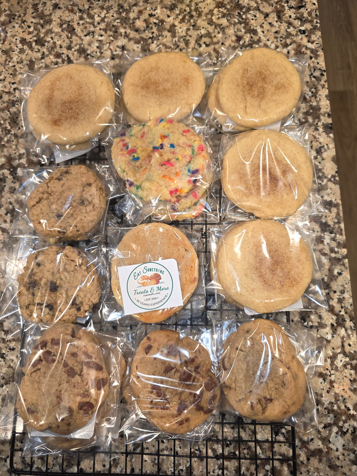 Twelve individually wrapped baked cookies, including several Oatmeal raisin chocolate chips, Snickerdoodles, and a colorful sprinkle Cookie